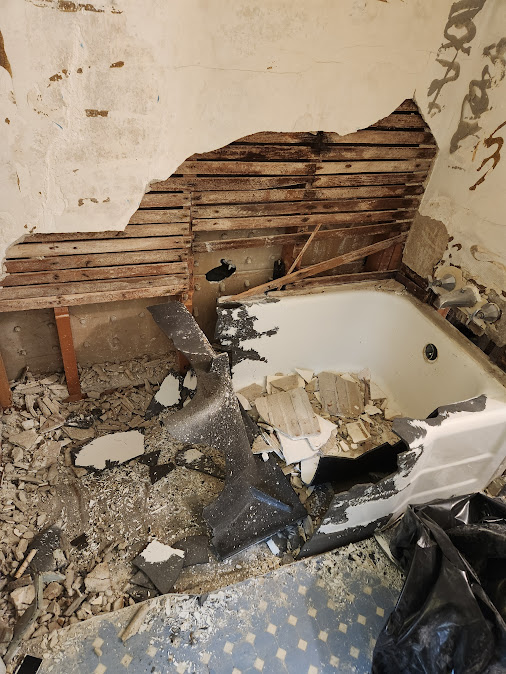 Bathroom demolition revealing damaged walls behind tub